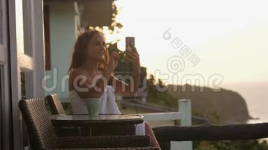 在<strong>日</strong>落时分，年轻女子在酒店阳台上用智能手机进行视频聊天，展示观看，分享旅游<strong>体验</strong>